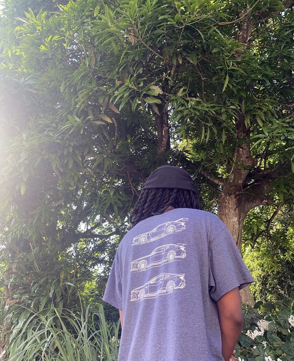 1NTERN from behind, in a T-shirt printed with race car outlines, under a tree