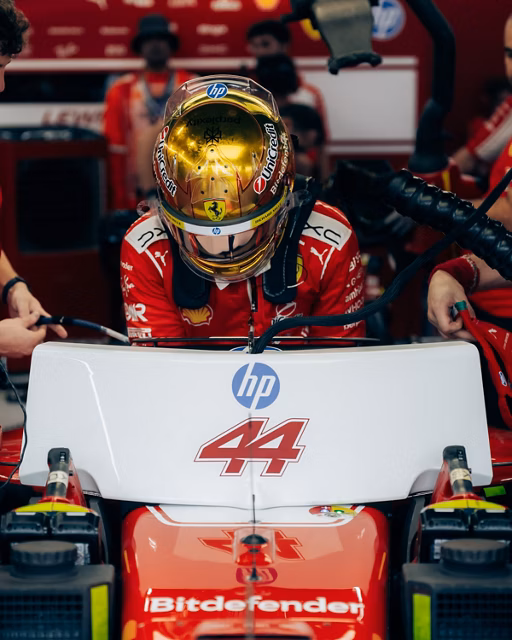 Lewis Hamilton in a gold helmet climbing into his number 44 Ferrari in the garage