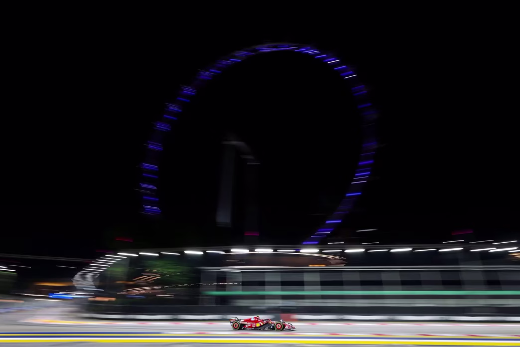 A Ferrari blurred by speed beneath the lit Singapore Flyer at night