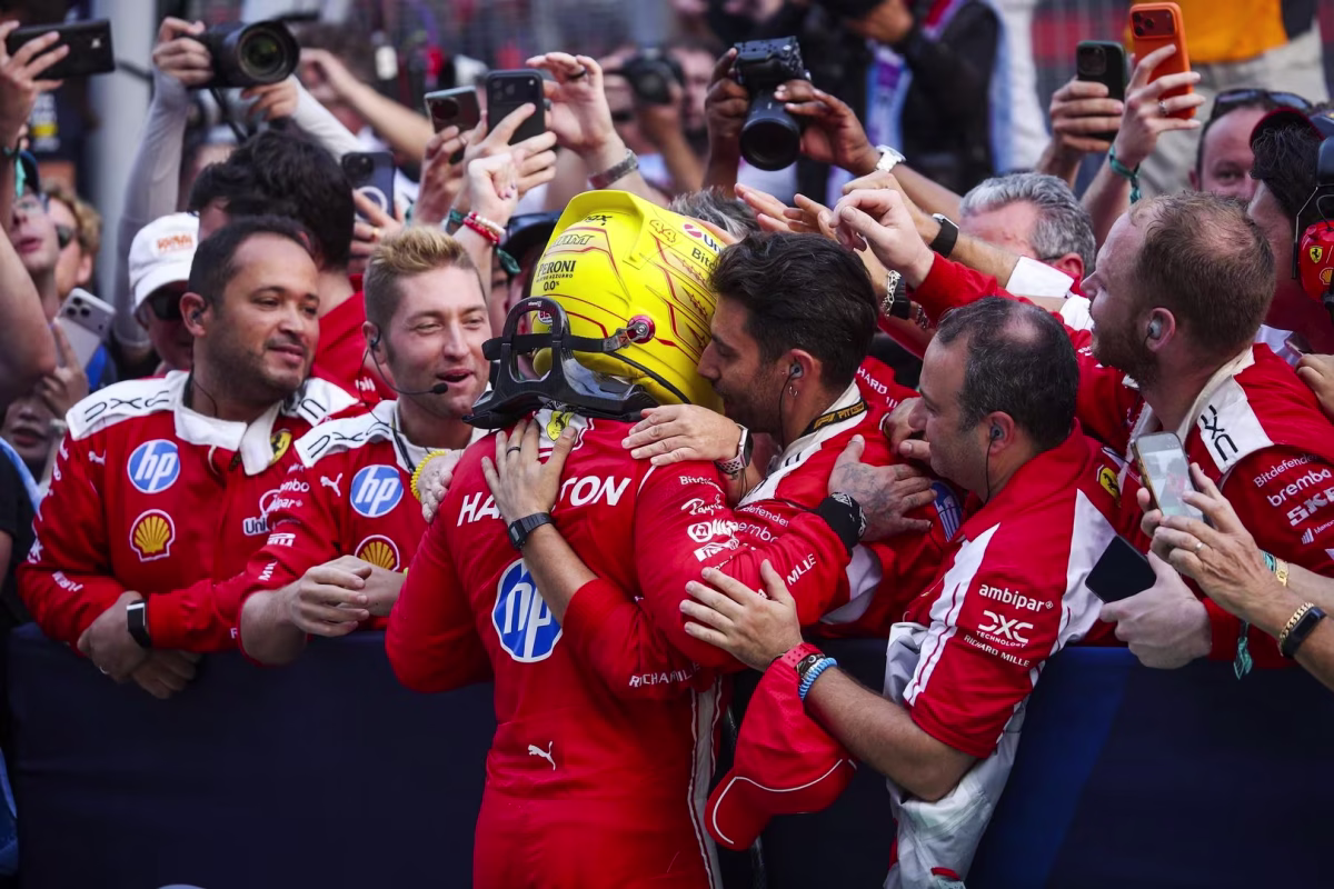 Lewis Hamilton, still in his yellow helmet, being hugged by Ferrari team members after finishing third at Sepang