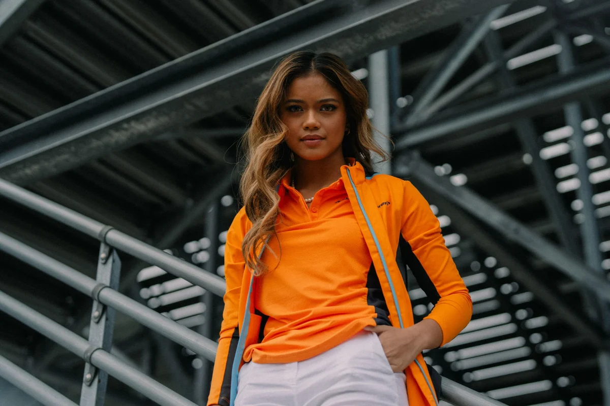 Bianca Bustamante in McLaren orange, standing on grandstand steps