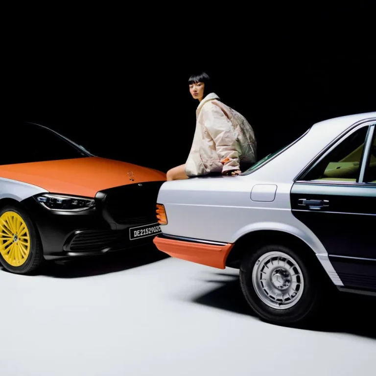 A model in a white look sitting on a classic Mercedes-Benz 500 SEL beside a newer S-Class with orange accents