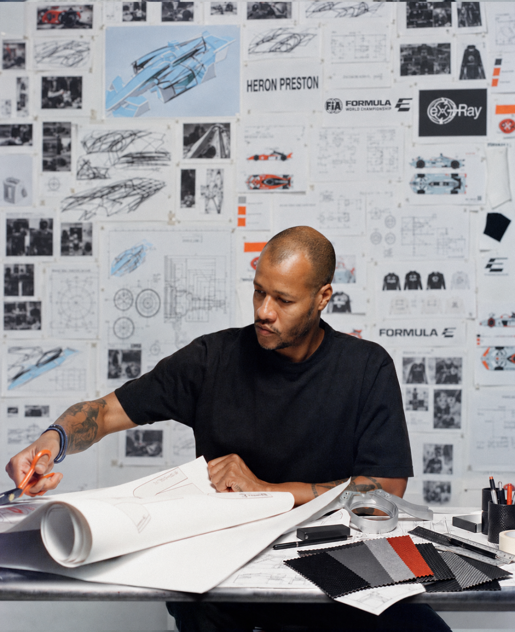 Heron Preston working at a desk in front of a wall of technical drawings