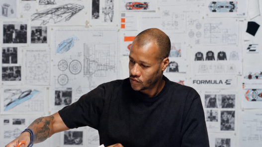 Heron Preston working at a desk in front of a wall of technical drawings