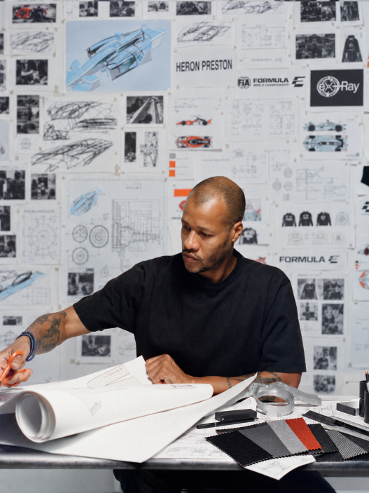 Heron Preston working at a desk in front of a wall of technical drawings