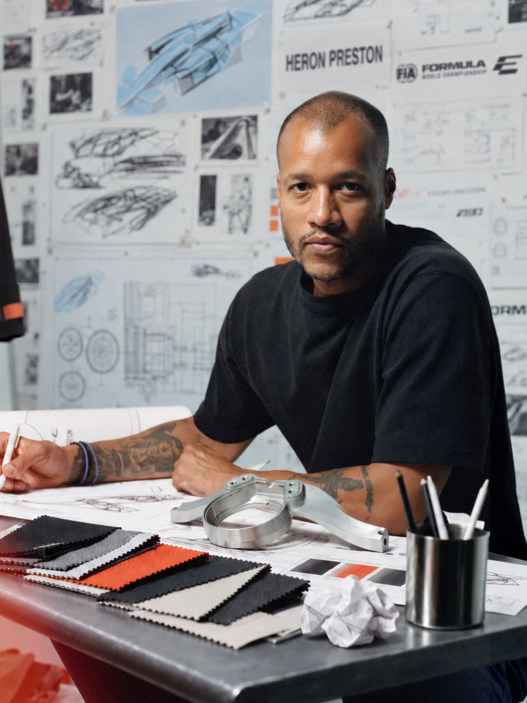 Heron Preston seated at a desk surrounded by sketches and reference sheets