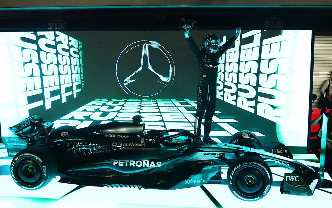 George Russell standing on his Mercedes in front of boards reading Russell