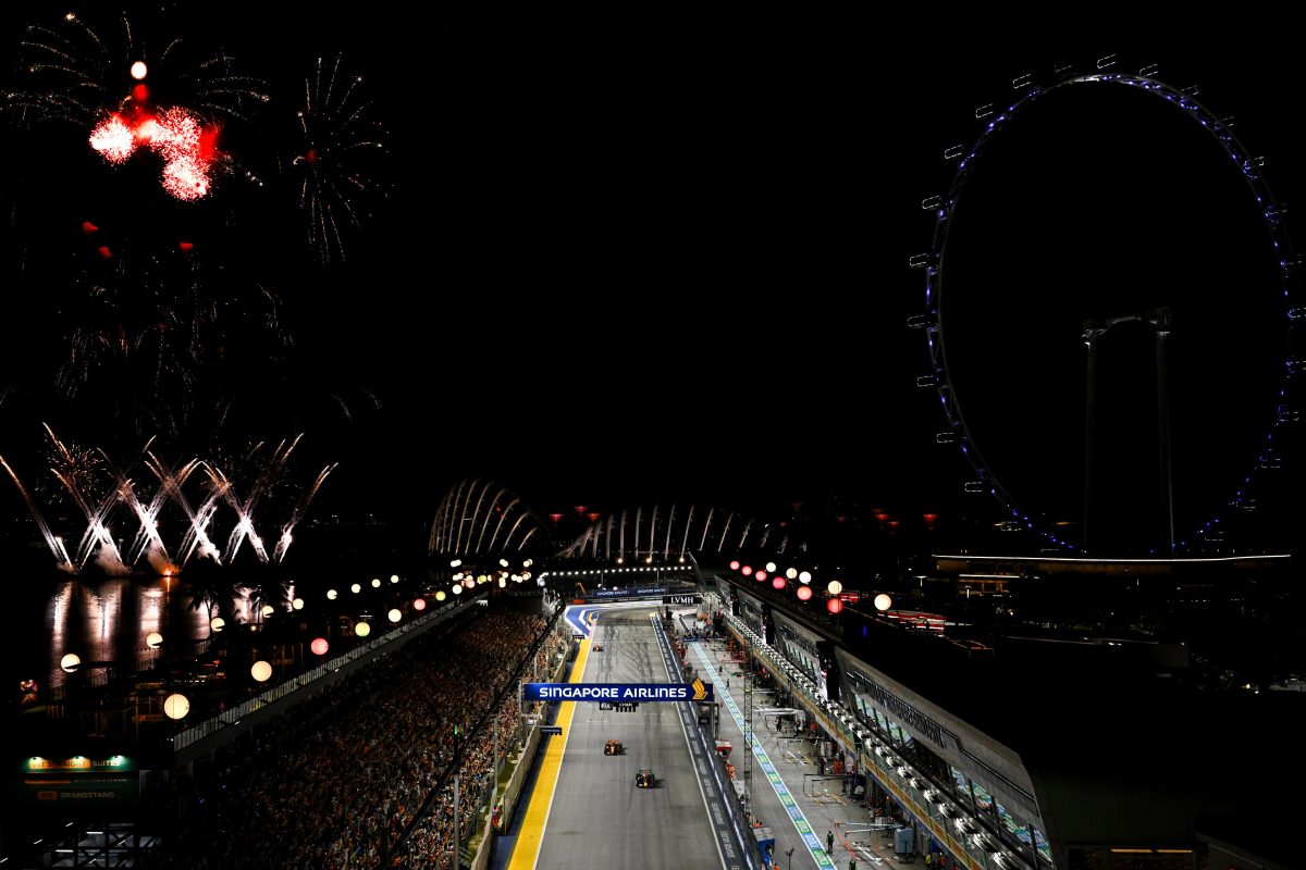 Fireworks over the Marina Bay Street Circuit as Max Verstappen leads Lando Norris at night, with the Singapore Flyer behind