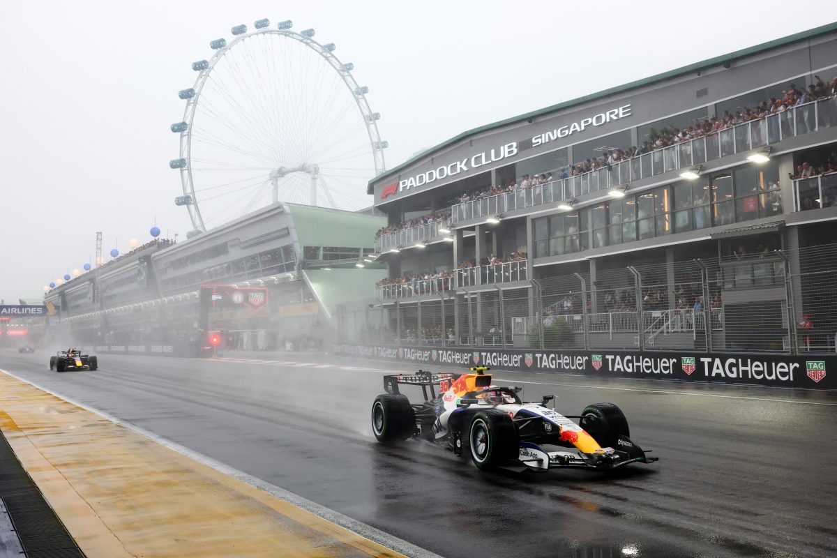 Liam Lawson’s Racing Bulls on a wet track past the Paddock Club, with the Singapore Flyer behind