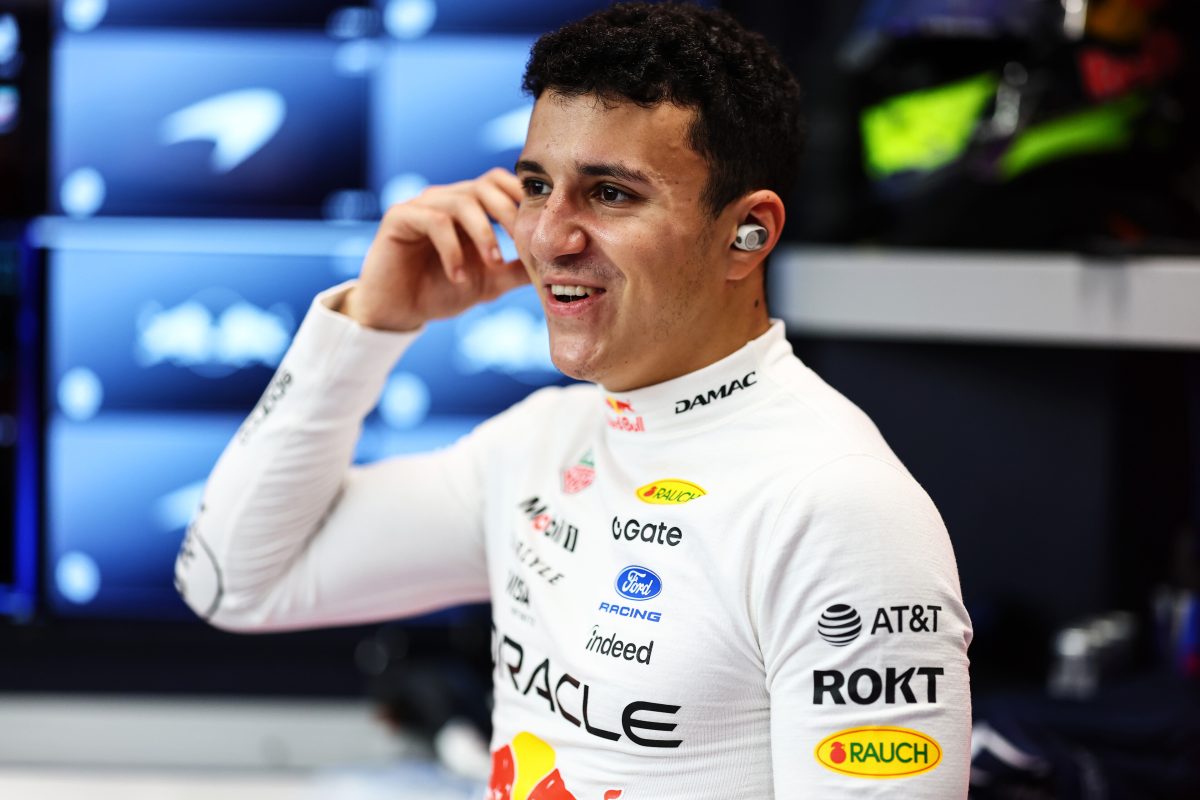 Isack Hadjar smiling with a hand to his earpiece in the Red Bull garage