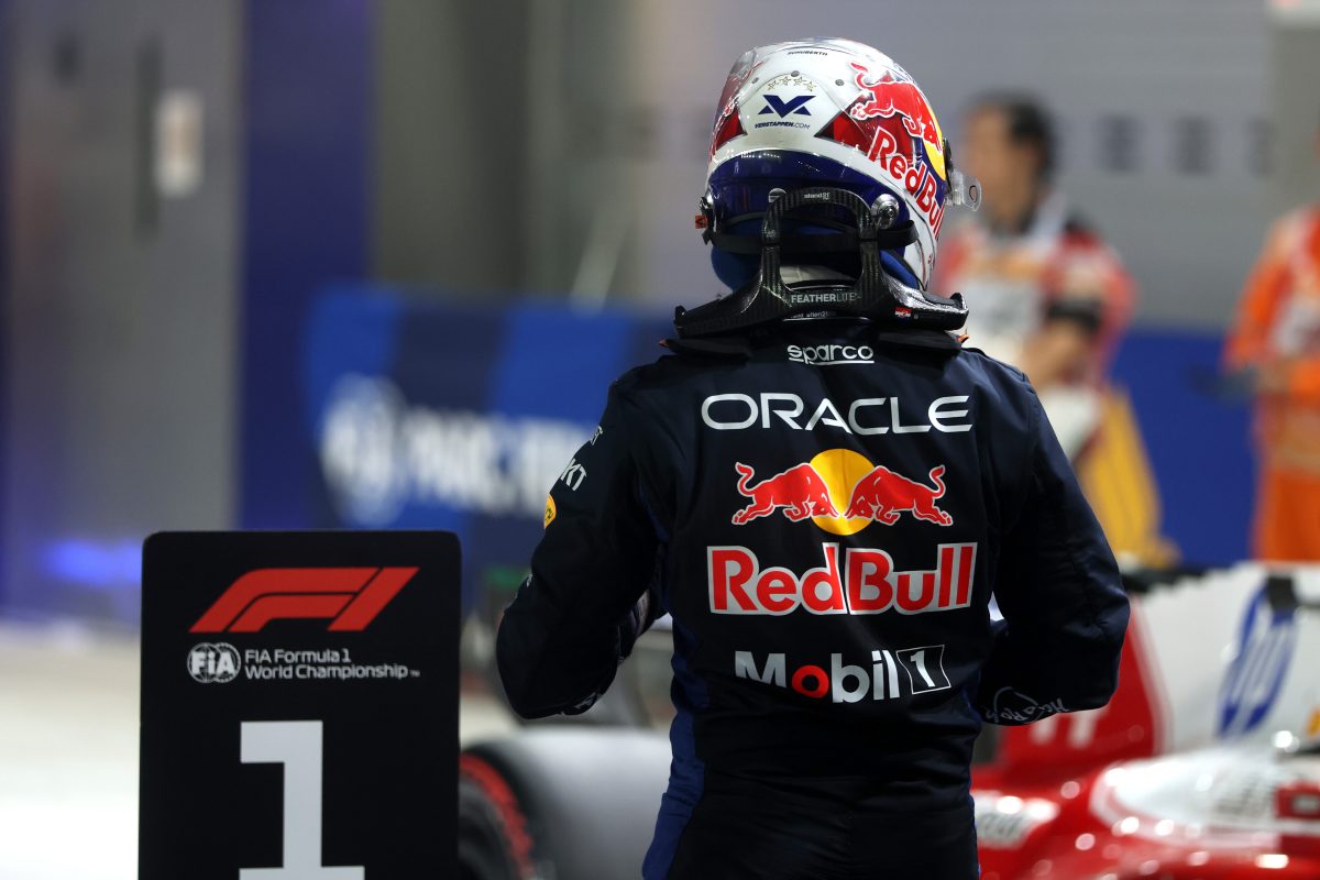 Max Verstappen seen from behind in his helmet and Red Bull race suit, beside the number 1 board in parc fermé