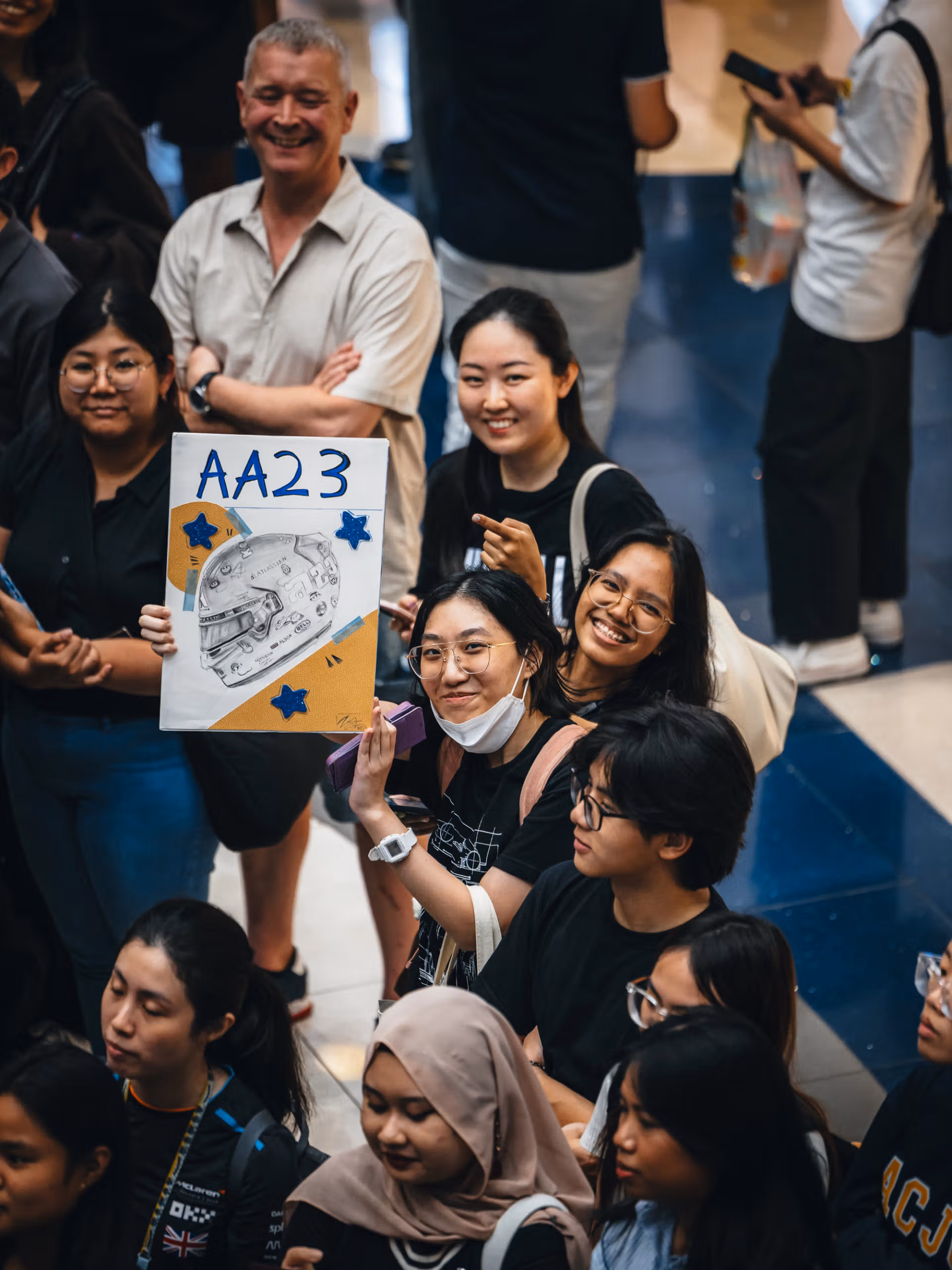 Fans smiling and holding a handmade AA23 sign with a drawing of Albon’s helmet