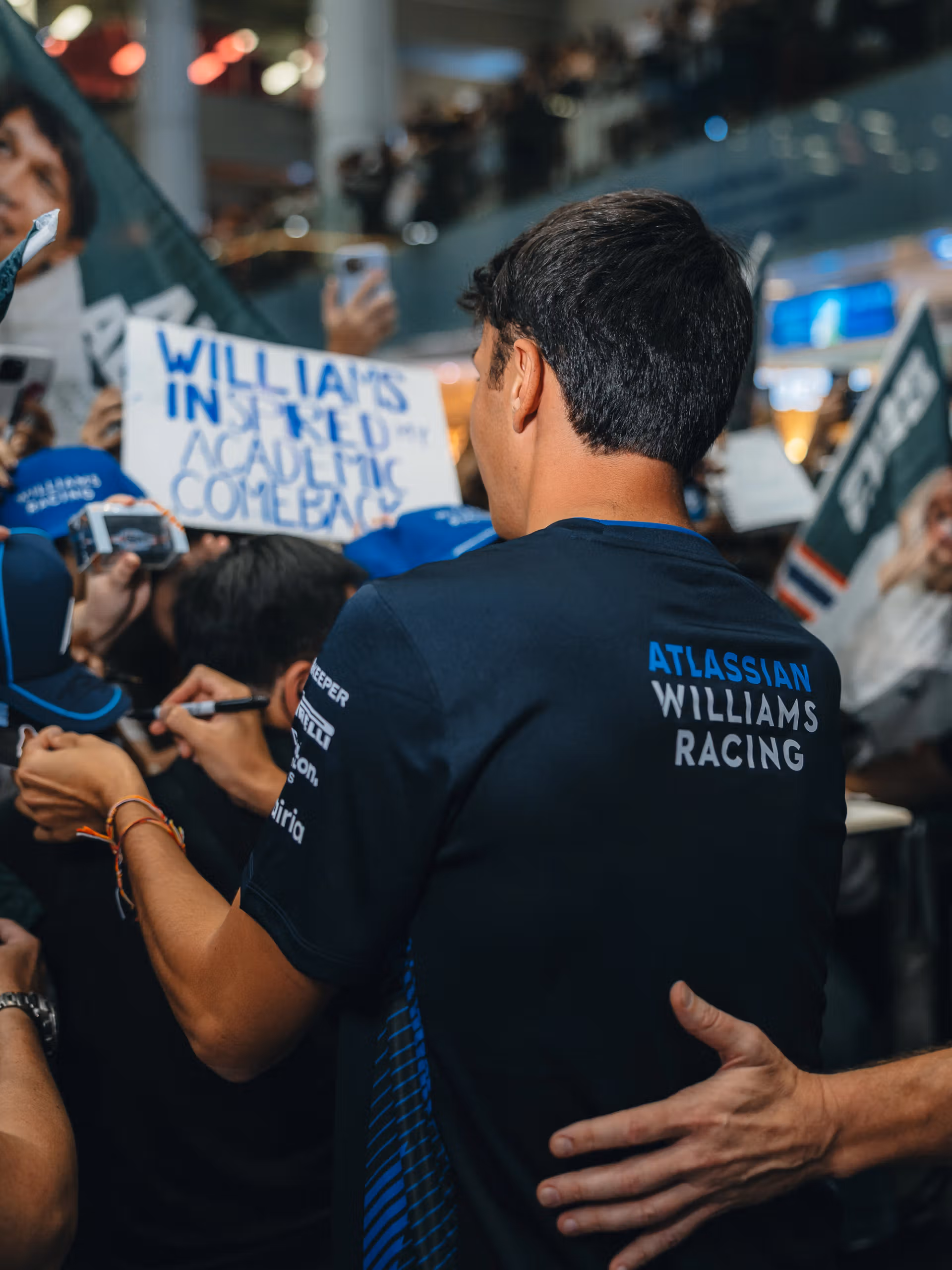 Alex Albon, in a Williams shirt, signing for a crowd of fans holding flags and a handmade sign