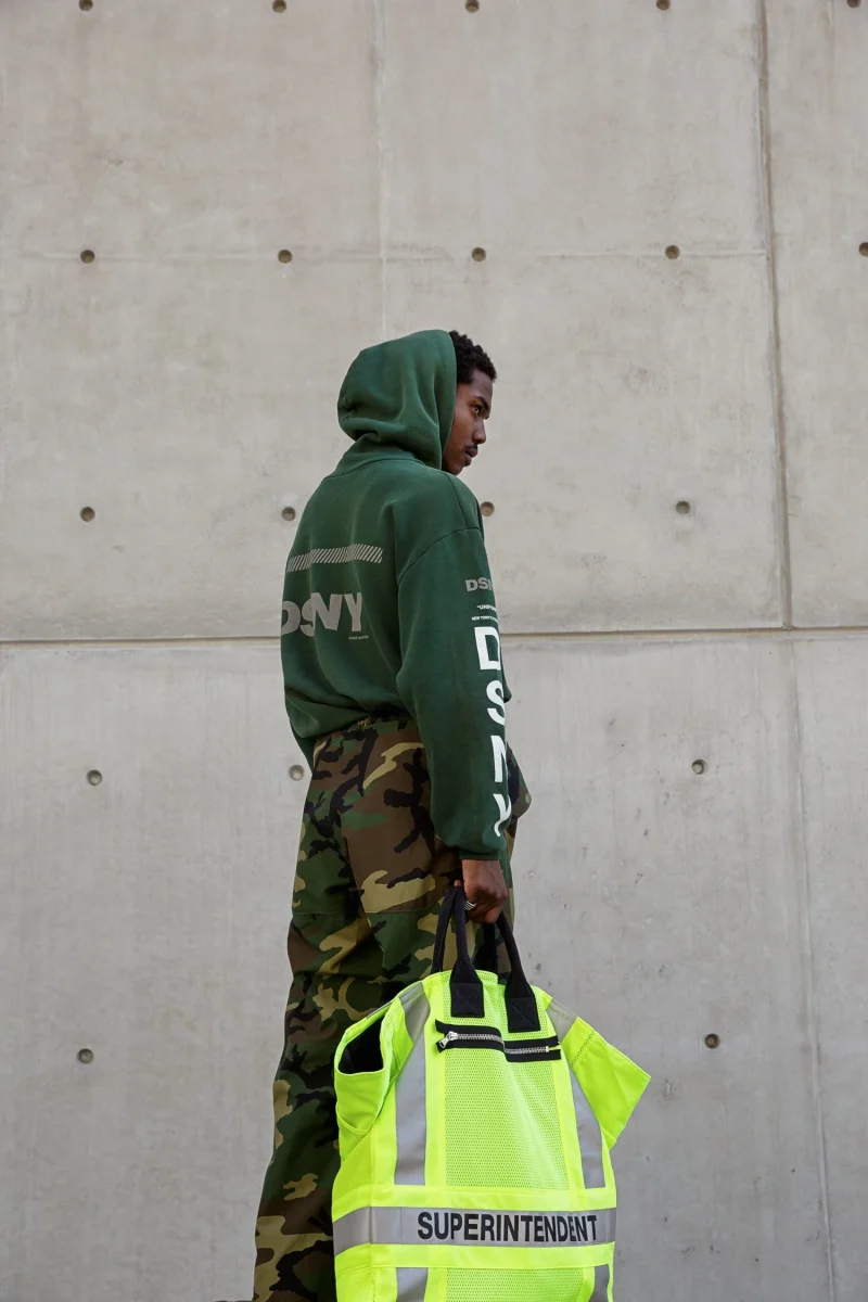 A model in a green DSNY hoodie and camouflage trousers carrying a high-visibility Superintendent bag