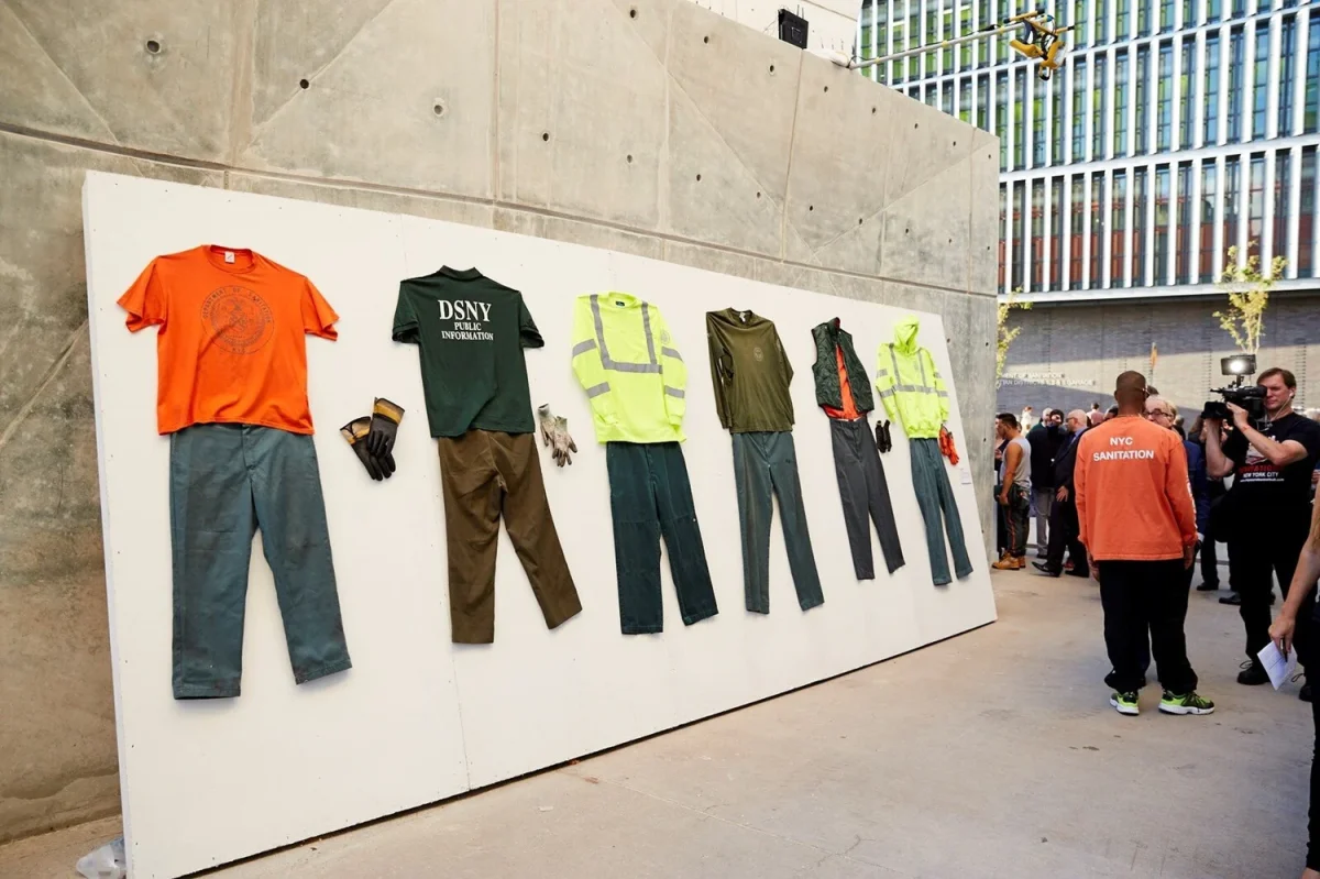 The UNIFORM installation outdoors, with sanitation workwear laid out on a white wall as visitors look on