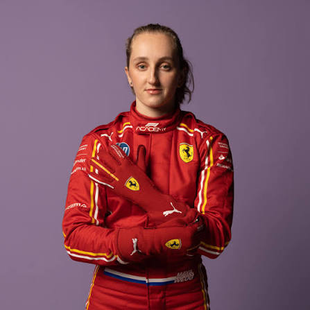 Maya Weug in a red Ferrari race suit, arms folded, against a lilac backdrop