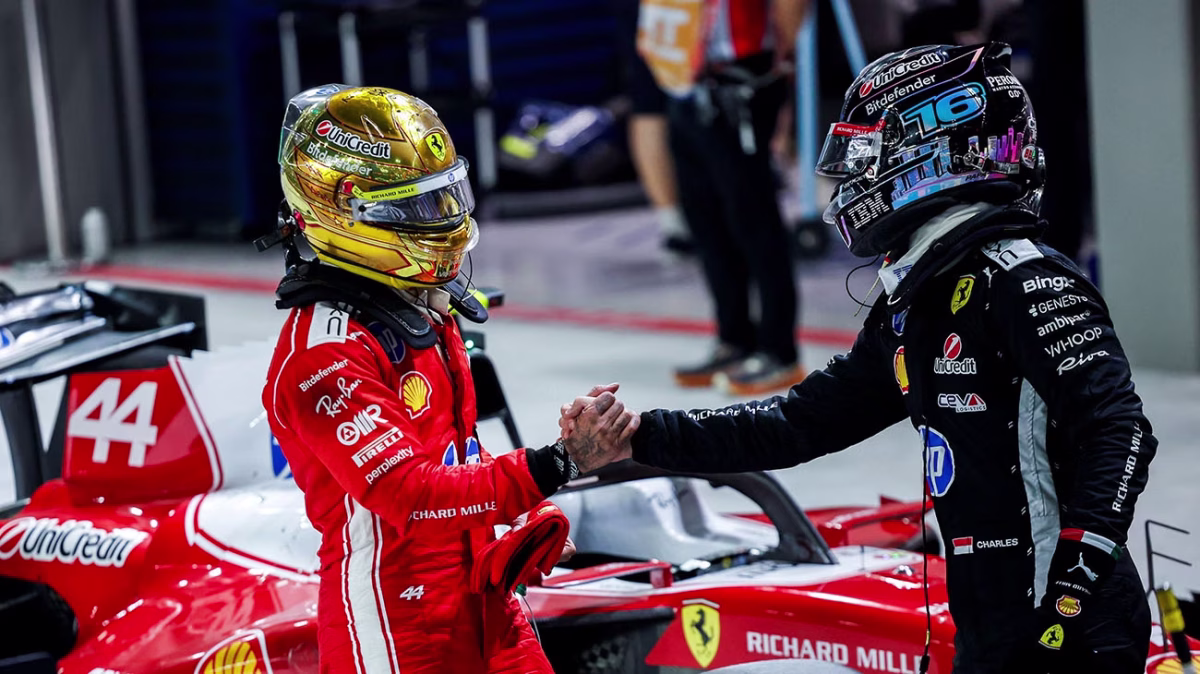 Lewis Hamilton in a gold helmet shaking hands with Charles Leclerc beside their Ferraris in parc fermé